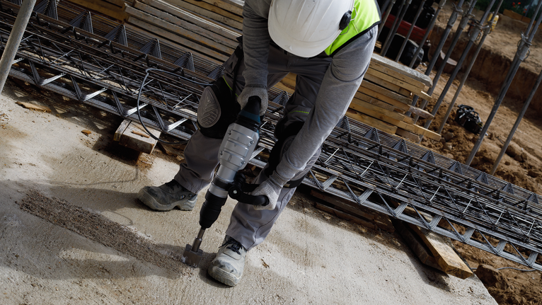 Uma pessoa usando equipamento de segurança perfura concreto em um canteiro de obras.