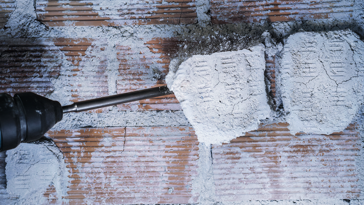 Um cinzel de martelo rotativo remove gesso de uma parede de tijolos.