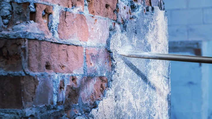 Cinzel removendo gesso de uma parede de tijolos em um ambiente de construção.