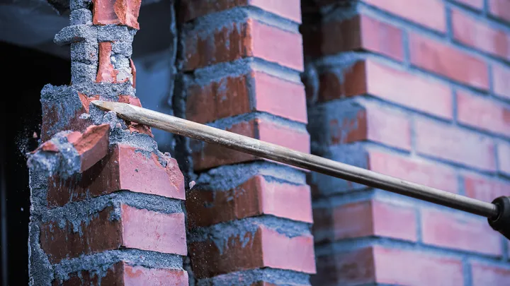 Ferramenta de cinzel quebrando tijolos vermelhos em um canteiro de obras.