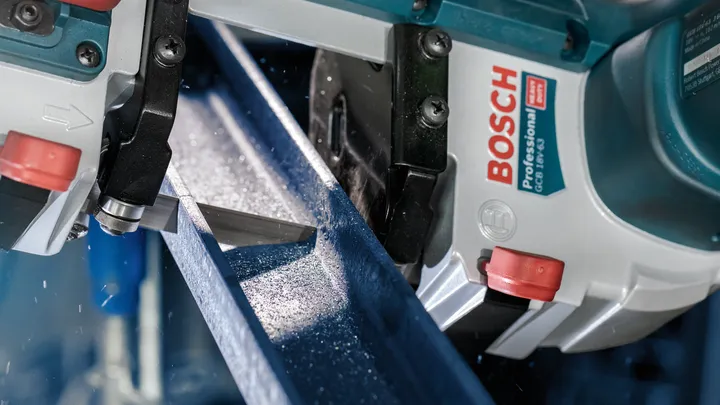 Serra de fita para metal corta uma viga de aço com pulverização de refrigerante.