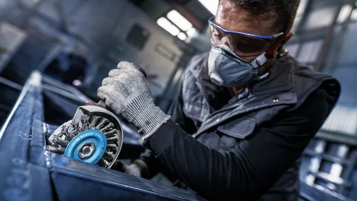 Uma pessoa usando equipamento de segurança tritura metal com uma escova de aço.