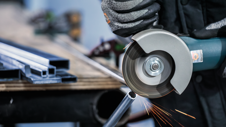 Uma pessoa usando equipamento de segurança corta um cano de metal com uma esmerilhadeira angular.