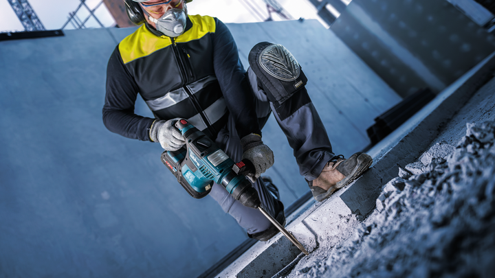 Uma pessoa usando equipamento de segurança perfura concreto em um canteiro de obras.