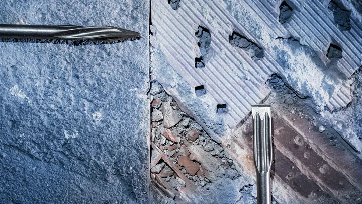Duas brocas de cinzel removendo concreto da superfície de uma parede.