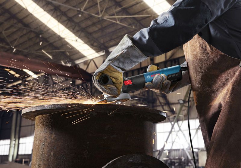 Uma pessoa usando equipamento de segurança tritura metal, produzindo faíscas em uma oficina.