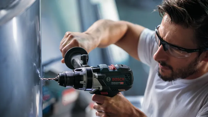 Pessoa usando equipamento de segurança perfura metal com uma ferramenta elétrica.