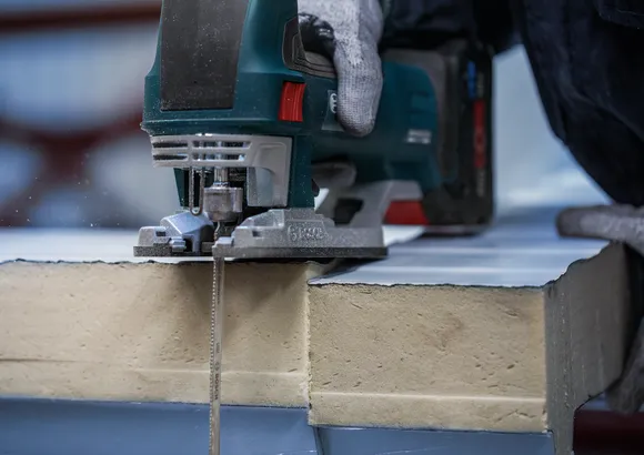 Pessoa usando equipamento de segurança corta placa de isolamento com uma serra tico-tico.