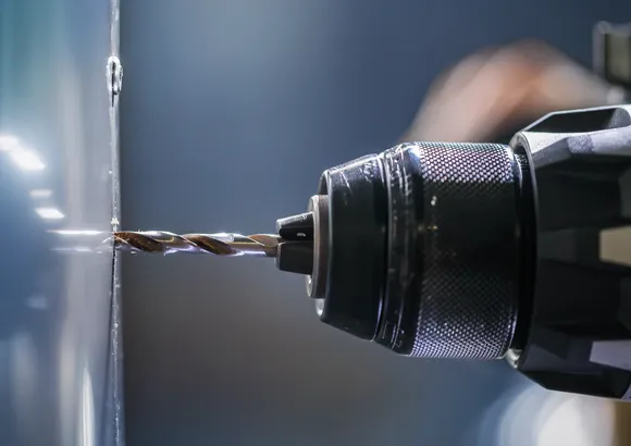 Uma furadeira elétrica fazendo um furo em uma superfície metálica.