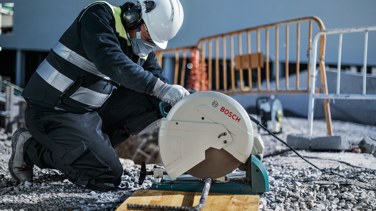 Um trabalhador usando equipamento de segurança corta vergalhões com uma serra circular em um canteiro de obras.