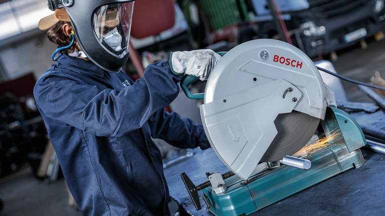 Uma pessoa usando equipamento de segurança está cortando um cano de metal com uma serra circular.