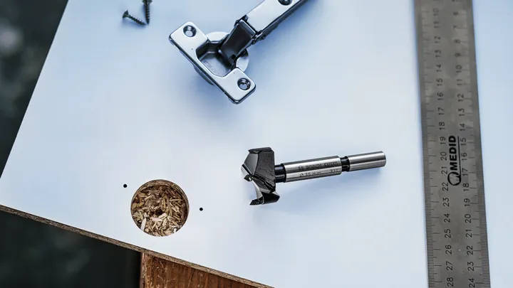 Broca Forstner, suporte e régua colocados em uma placa com um furo perfurado.