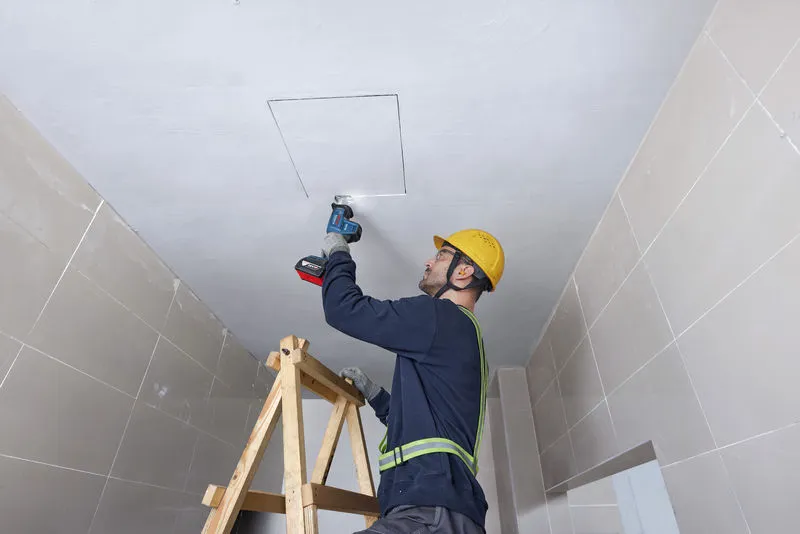 Uma pessoa usando equipamento de segurança usa uma serra alternativa para cortar um painel de teto.