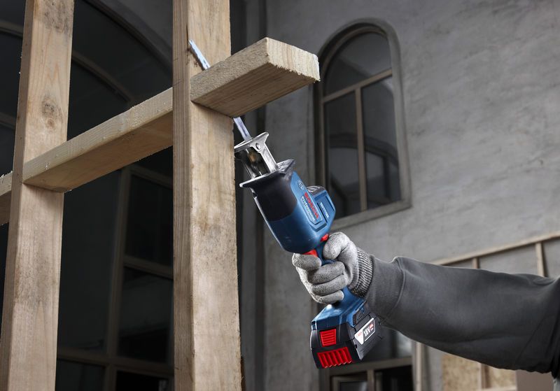 Uma pessoa usando equipamento de segurança usa uma serra alternativa para cortar vigas de madeira.