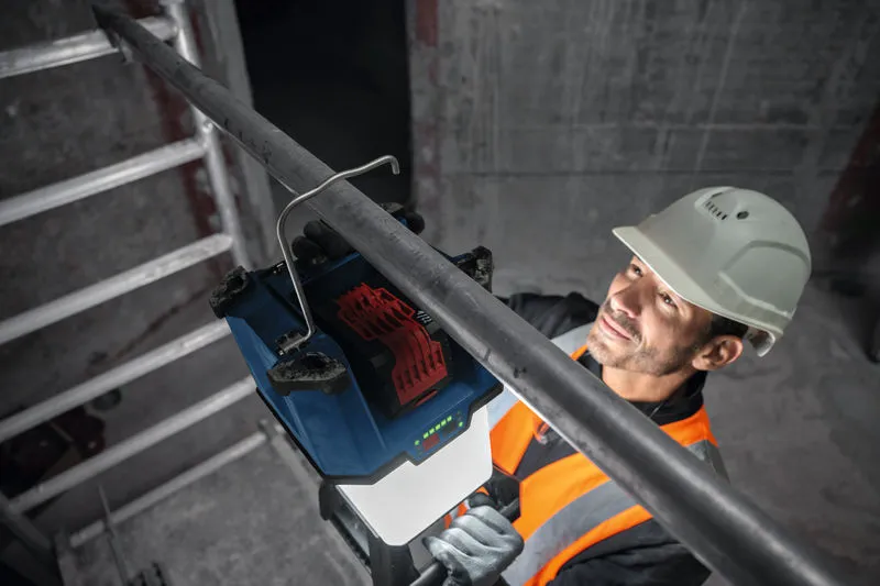 Uma pessoa usando equipamento de segurança monta uma luz de trabalho sem fio em um tubo de metal.