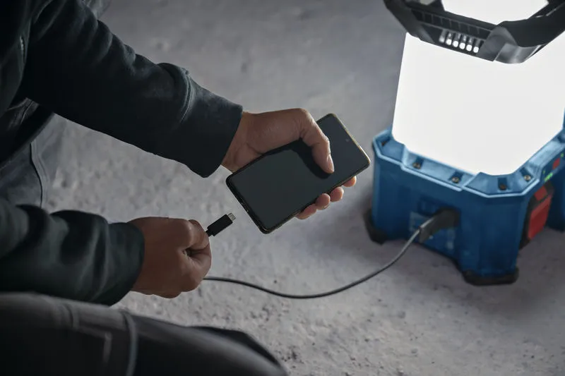 Pessoa carregando um smartphone usando uma luz de trabalho sem fio em um piso de concreto.