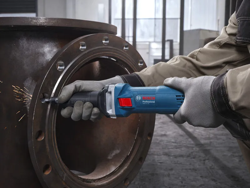 Uma pessoa usando equipamento de segurança tritura um tubo de metal com uma retificadora reta.