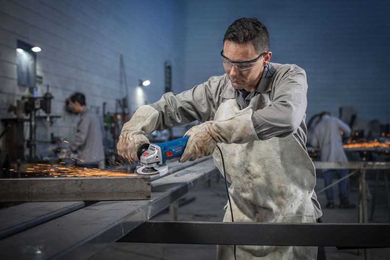 Uma pessoa usando equipamento de segurança tritura metal com uma esmerilhadeira angular, produzindo faíscas.