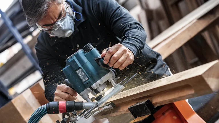 Pessoa usando equipamento de segurança apara madeira com uma tupia elétrica.