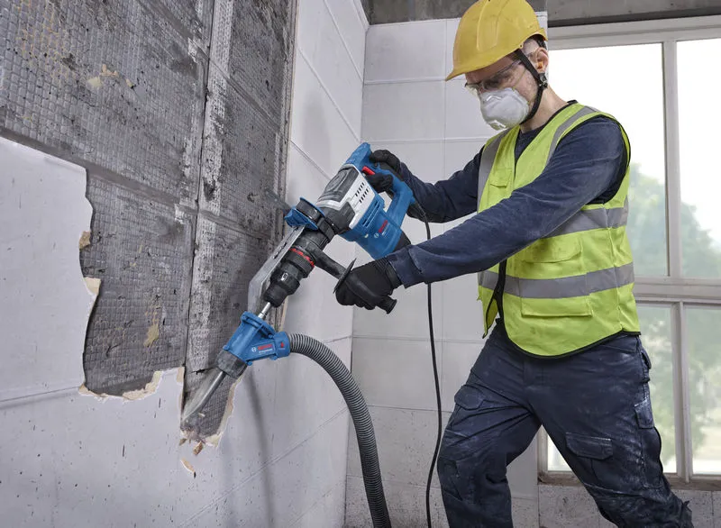 Um trabalhador usando equipamento de segurança usa um martelo de demolição com SDS Max em uma parede de azulejos.