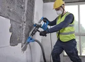 Um trabalhador usando equipamento de segurança usa um martelo de demolição com SDS Max em uma parede de azulejos.