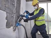 Um trabalhador usando equipamento de segurança usa um martelo de demolição com SDS Max em uma parede de azulejos.