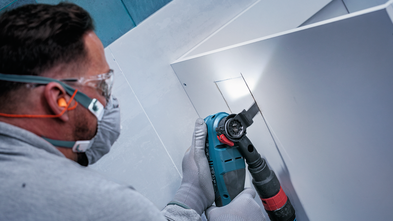 Pessoa usando equipamento de segurança corta um painel com uma ferramenta elétrica.