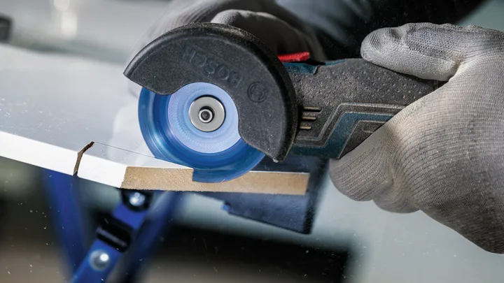 Uma pessoa usando equipamento de segurança usa uma serra circular para cortar uma folha de material.