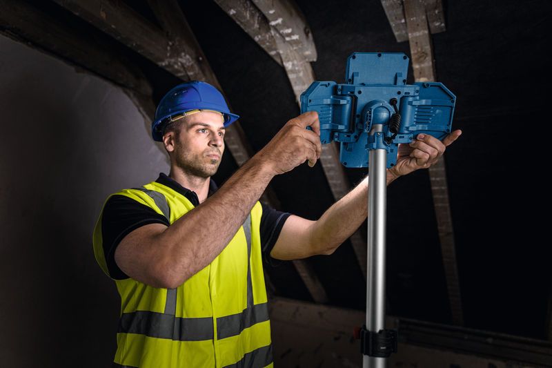 Um trabalhador usando equipamento de segurança ajusta uma luminária sem fio de obra em um suporte.