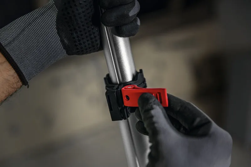 Uma pessoa usando equipamento de segurança ajusta uma braçadeira vermelha em um poste de metal.