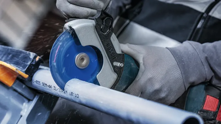 Uma pessoa usando equipamento de segurança corta um cano de plástico com uma serra circular.