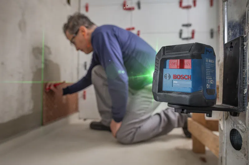 A ferramenta de nivelamento a laser projeta linhas verdes enquanto uma pessoa ajusta os azulejos na parede.