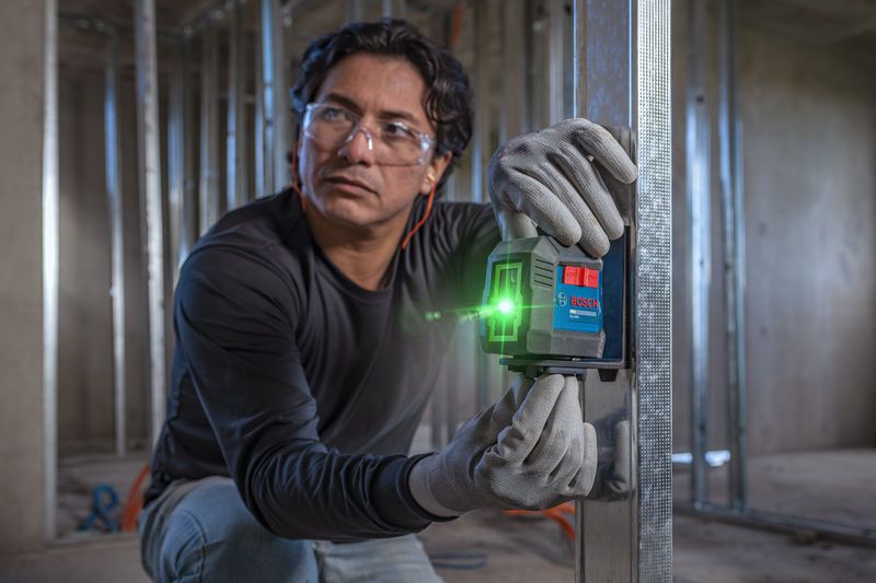 Uma pessoa usando equipamento de segurança alinha uma ferramenta de nivelamento a laser em uma estrutura metálica.