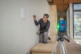 Uma pessoa marca uma parede usando um nivelador a laser, projetando linhas verdes.