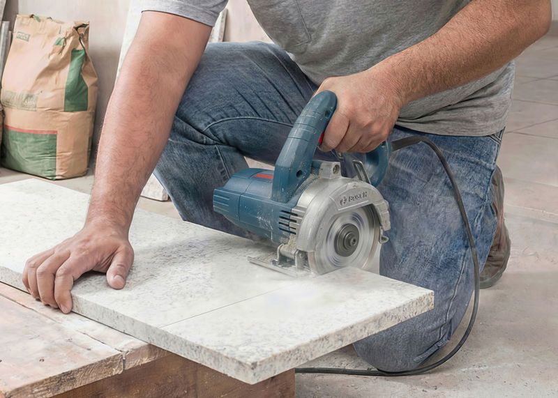 Uma pessoa corta um azulejo usando uma cortadora de azulejos diamantada em uma bancada.