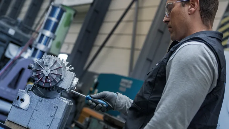 Pessoa usando equipamento de segurança aperta um parafuso em máquina industrial.