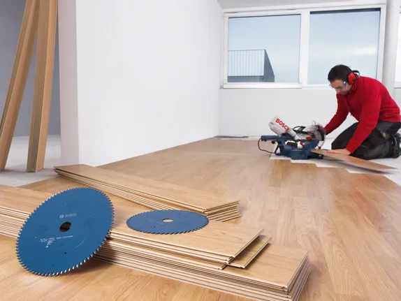 Trabalhador usando equipamento de segurança corta piso laminado com uma serra de esquadria.