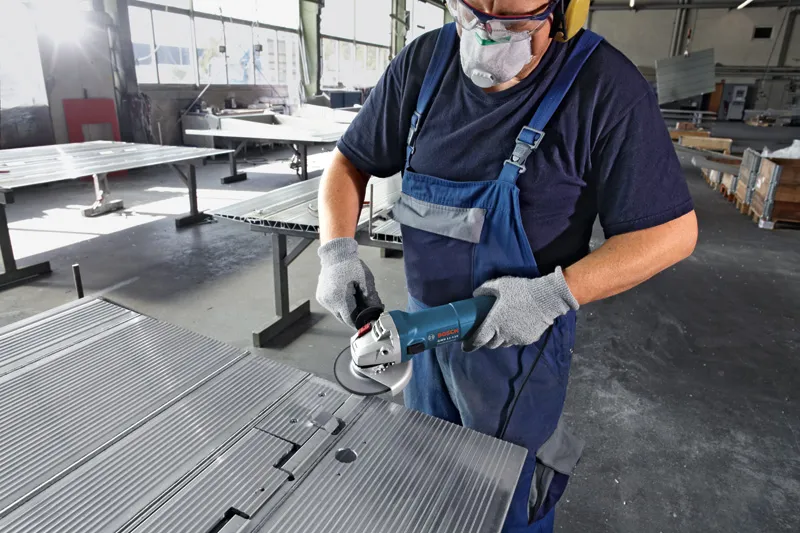 Uma pessoa usando equipamento de segurança esmerilha uma chapa de metal com uma esmerilhadeira angular.