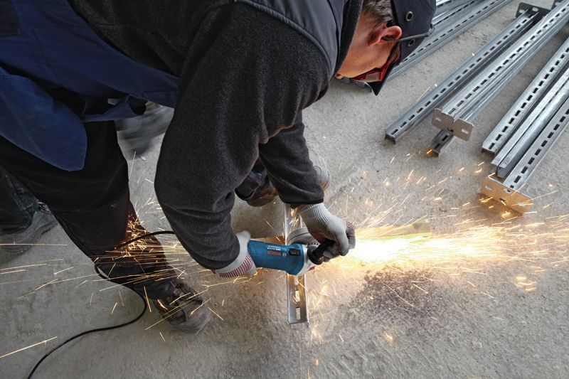 Uma pessoa usando equipamento de segurança tritura uma viga de metal, produzindo faíscas brilhantes.