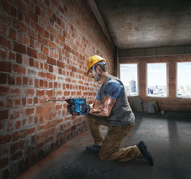 Una persona que usa equipo de seguridad perfora una pared de ladrillos dentro de un edificio en construcción.