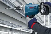 Una persona que usa equipo de seguridad perfora una viga de metal con una herramienta eléctrica.
