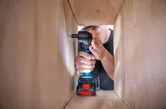 Una persona que usa equipo de seguridad utiliza un taladro inalámbrico para colocar un tornillo dentro de un marco de madera.