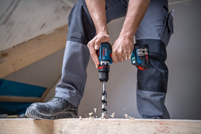 Una persona que usa equipo de seguridad perfora madera con un taladro inalámbrico.