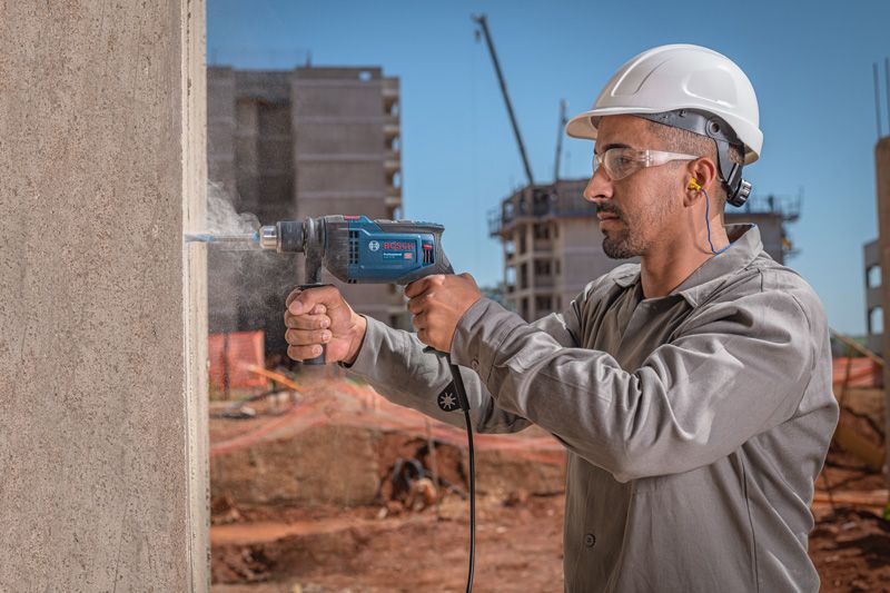 Una persona que usa equipo de seguridad perfora una pared de hormigón en un sitio de construcción.