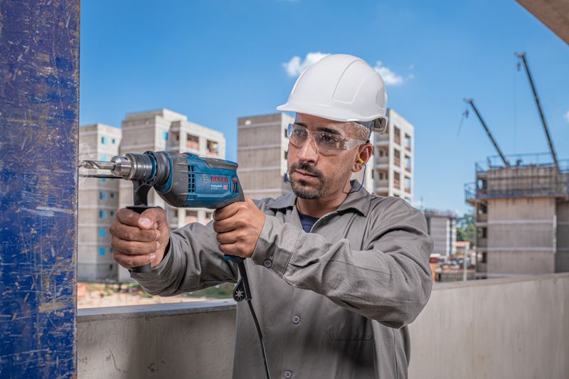Una persona que usa equipo de seguridad utiliza un taladro de impacto sobre una viga de acero en un sitio de construcción.