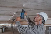 Una persona que usa equipo de seguridad perfora un techo de concreto usando un taladro de impacto.