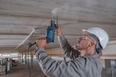 Una persona que usa equipo de seguridad perfora un techo de concreto usando un taladro de impacto.