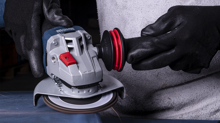 Una persona que usa equipo de seguridad utiliza una amoladora angular para cortar metal.