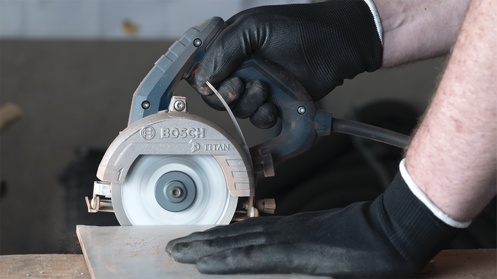 Persona que usa equipo de seguridad corta una baldosa con una sierra circular.