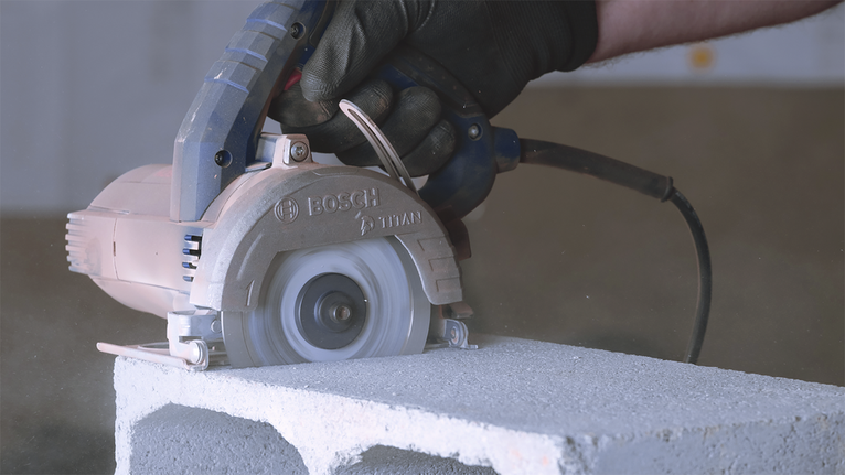 Una persona que usa equipo de seguridad utiliza una sierra circular para cortar un bloque de hormigón.